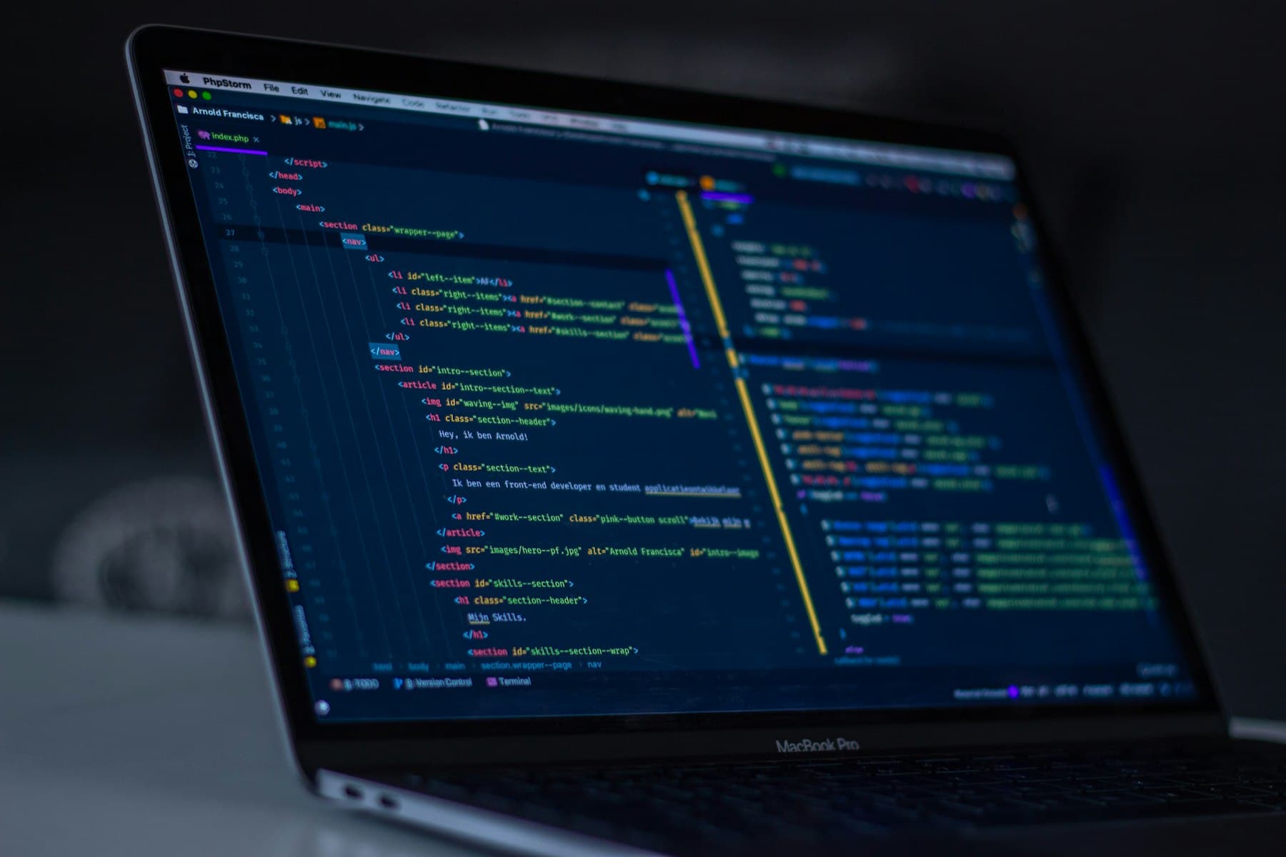 A laptop in a dark room showing a code editor with syntax-highlighted PHP